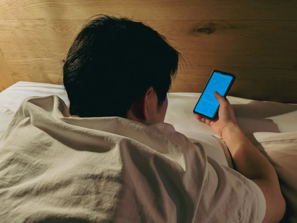 ベッドで横になりながらスマートフォンを操作する人