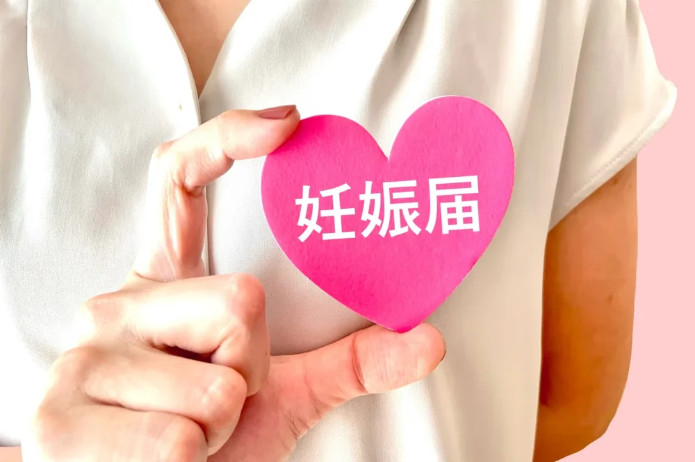 「妊娠届」と書かれたハート型の紙を持つ手