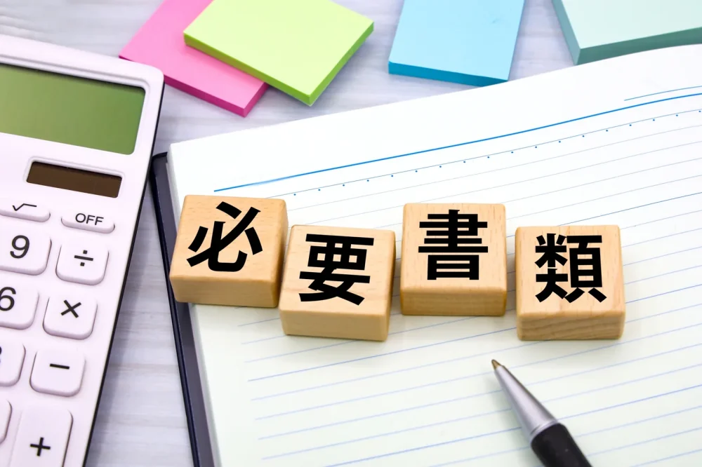 「必要書類」と書かれた木製ブロックと電卓