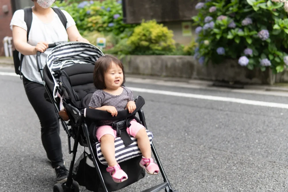 ベビーカーに乗る子どもと歩く母親